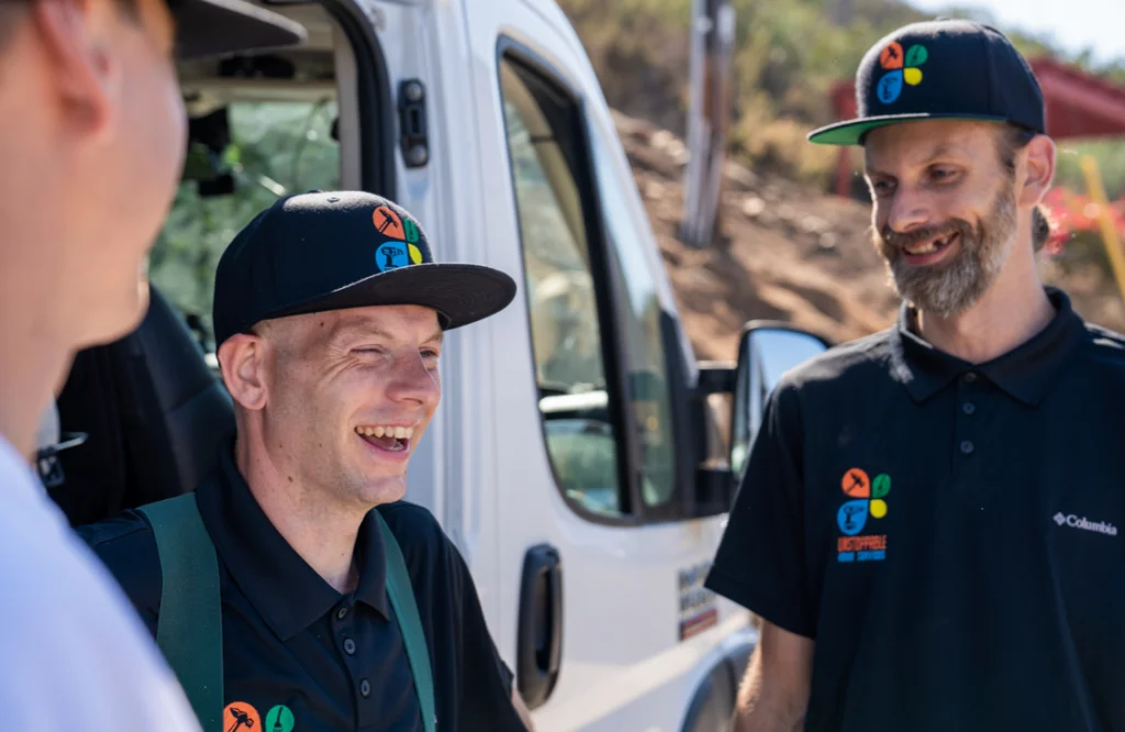 Three handyman pros smiling outside in front of work van