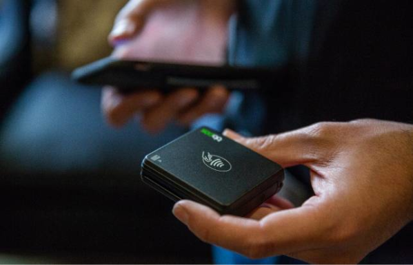 Person holding black card reader in left hand and mobile phone in right