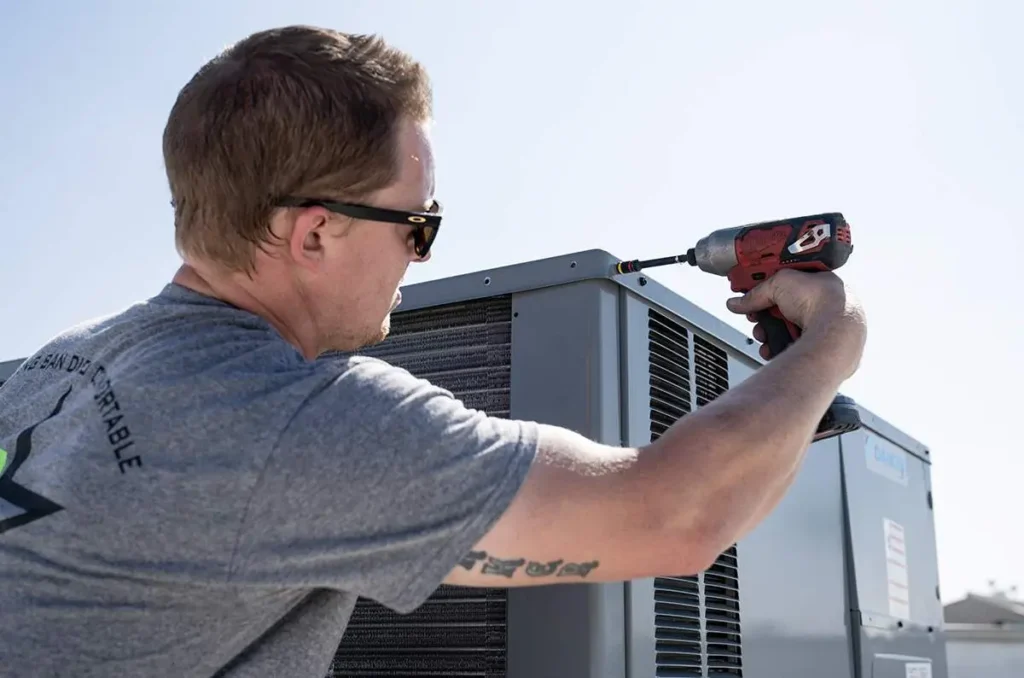 Service technician using power tool drill to unscrew HVAC unit